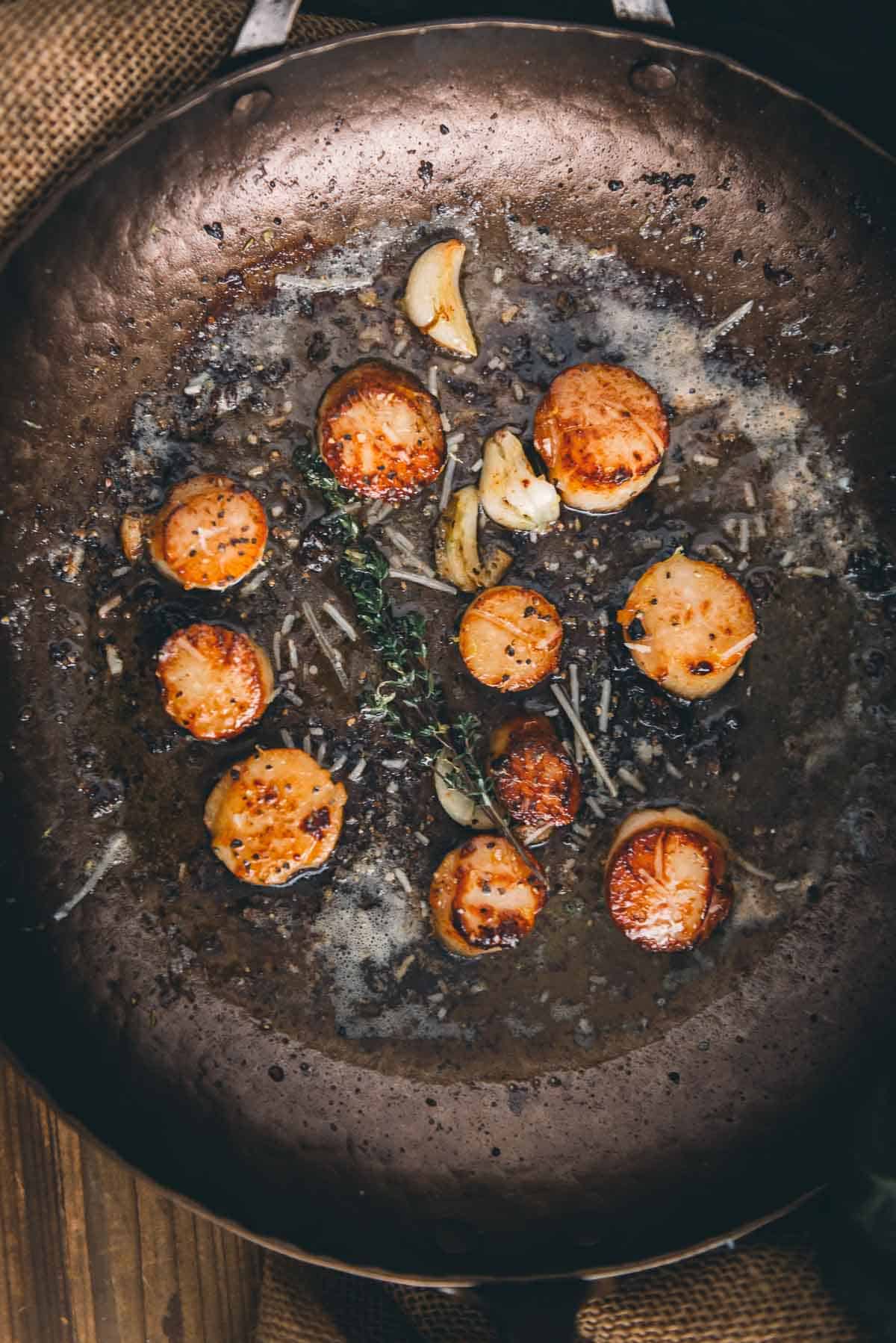 Scallops in a frying pan on a wooden table.