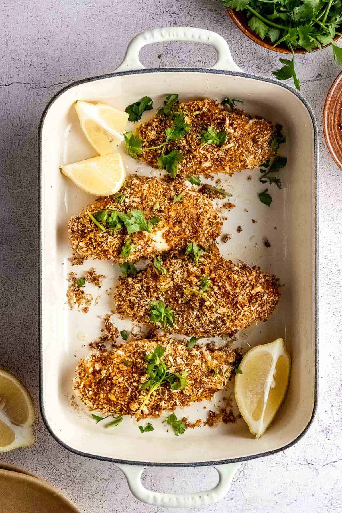 Baked crusted chicken in a baking dish with lemon wedges.