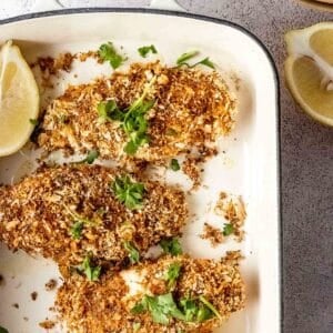 Baked panko crusted chicken breasts in a baking dish with lemon wedges.