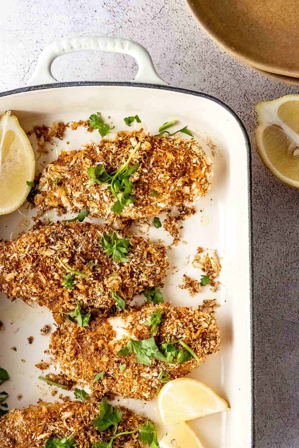 Baked panko crusted chicken breasts in a baking dish with lemon wedges.