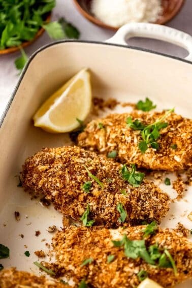 Parmesan panko crusted chicken breasts in a baking dish with lemon and parsley.