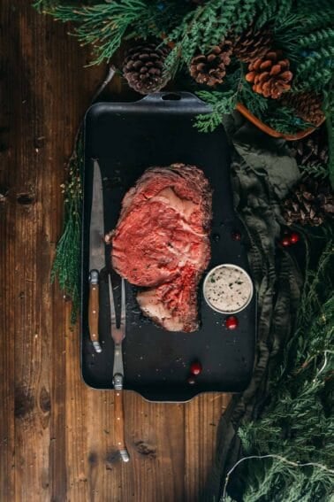 A slice of smoked prime rib on a black tray with a knife and fork.