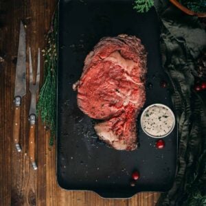 A slice of prime rib on a tray with a knife and fork on a wooden table.