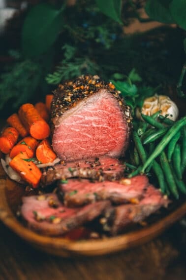 Steak on a wooden plate with carrots and green beans.