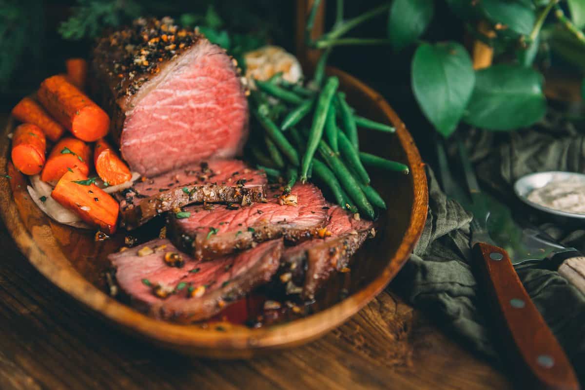 A plate of beef, carrots, and green beans on a wooden table.
