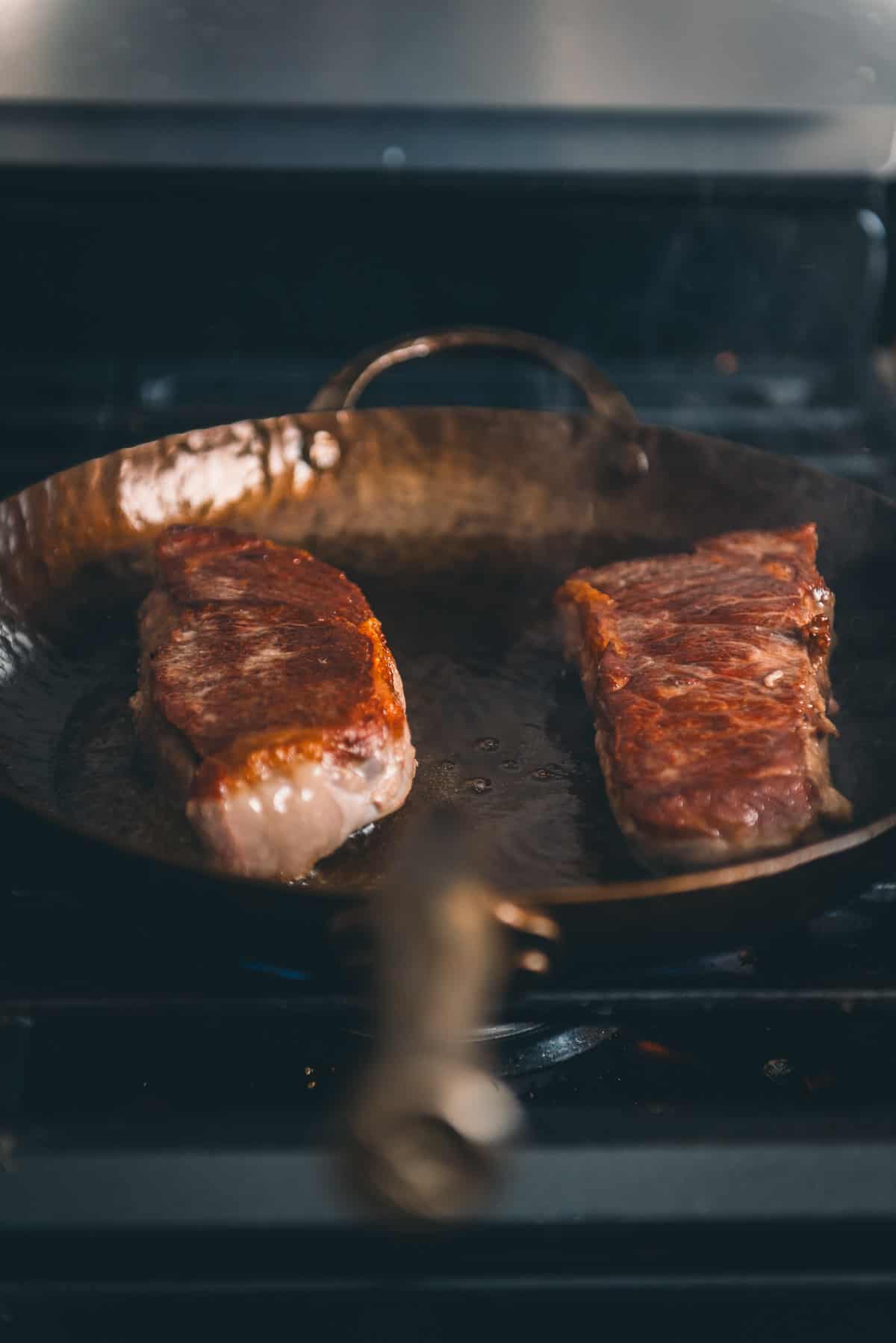 Two strip steaks in a frying pan on the stove.