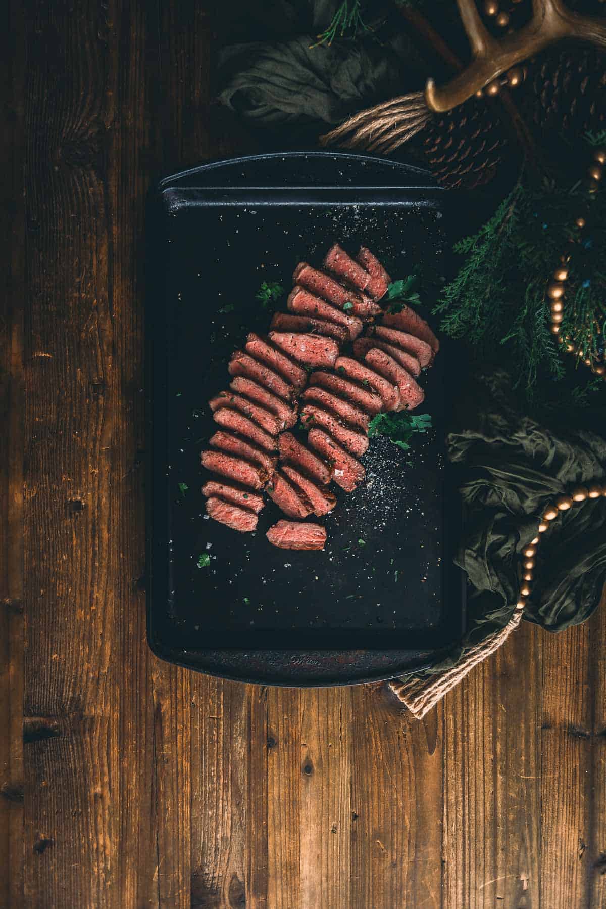 Strip steak on a black plate on a wooden table.