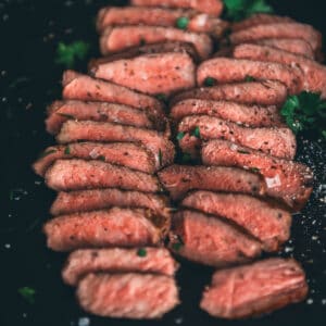 Sliced strip steak on a black baking sheet.