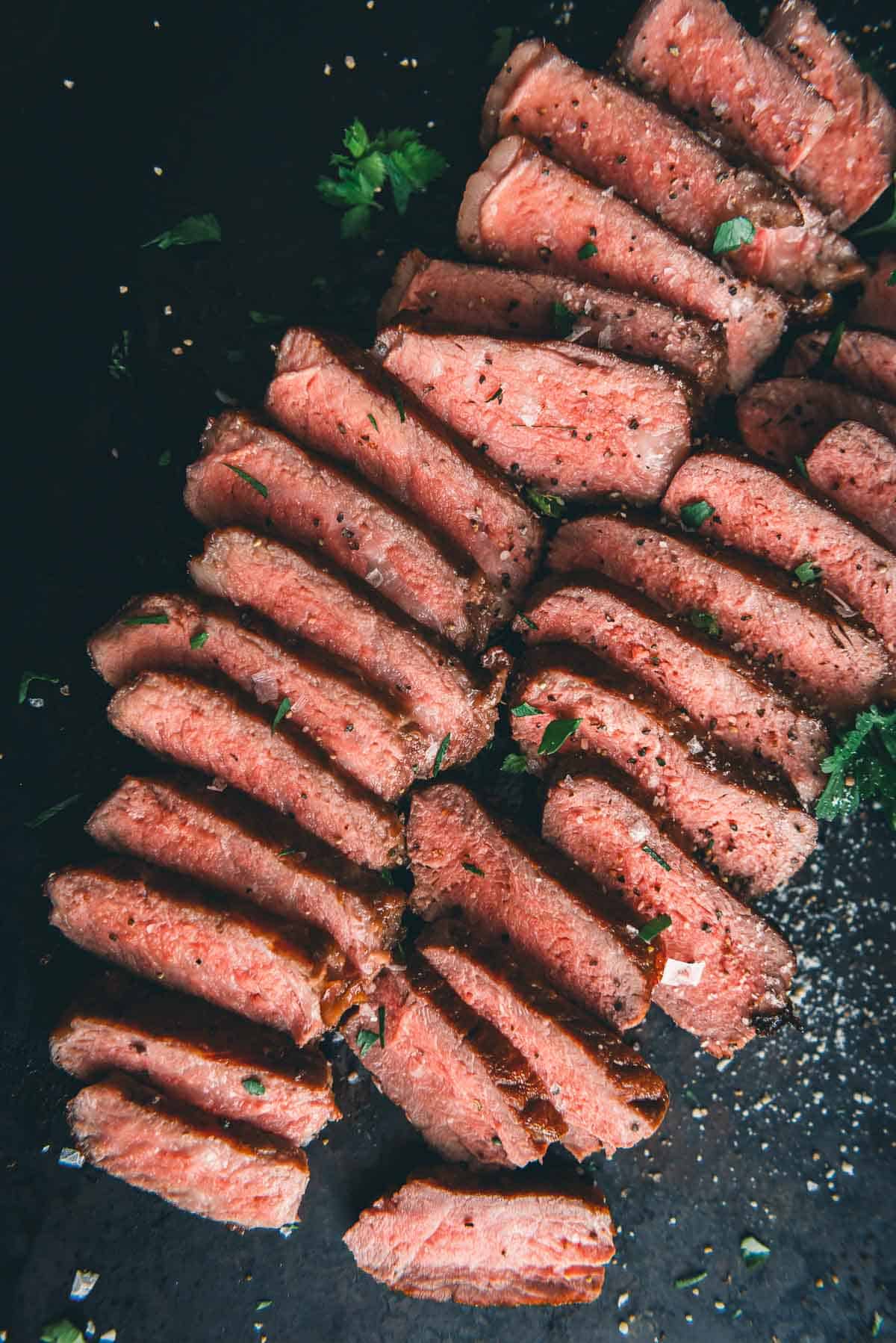 Sliced New york strip steak on a black plate.