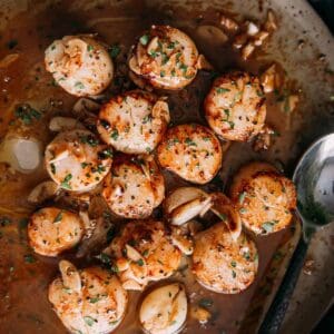 Golden brown seared Scallops in a pan with garlic and herbs.