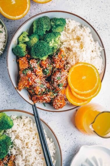 Air fryer orange chicken with sesame seeds in a bowl with side dishes.