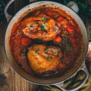 Braised pork shanks in a thick sauce in a pan on a wooden table.