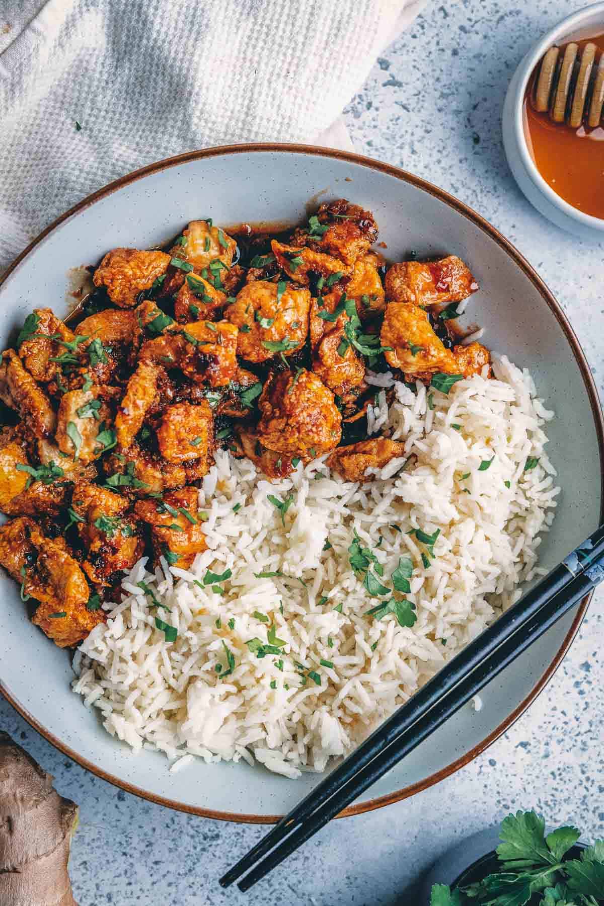 A bowl of chicken and rice with a spoon and chopsticks.