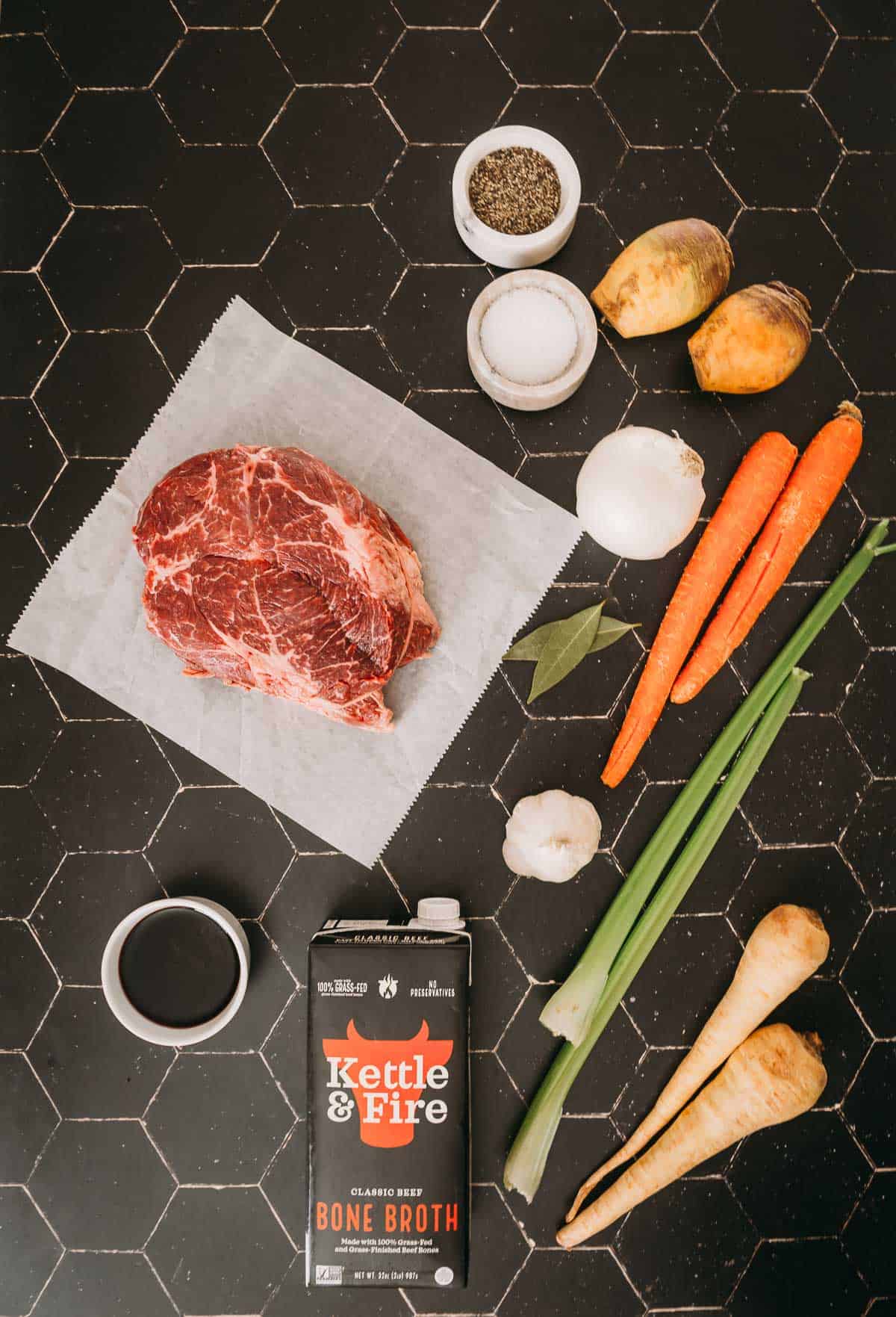 Meat, carrots, and other ingredients on a black countertop.