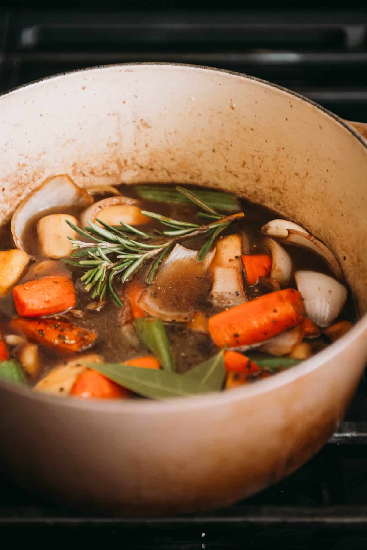 A Dutch oven of broth with carrots, onions, and sprigs of rosemary.