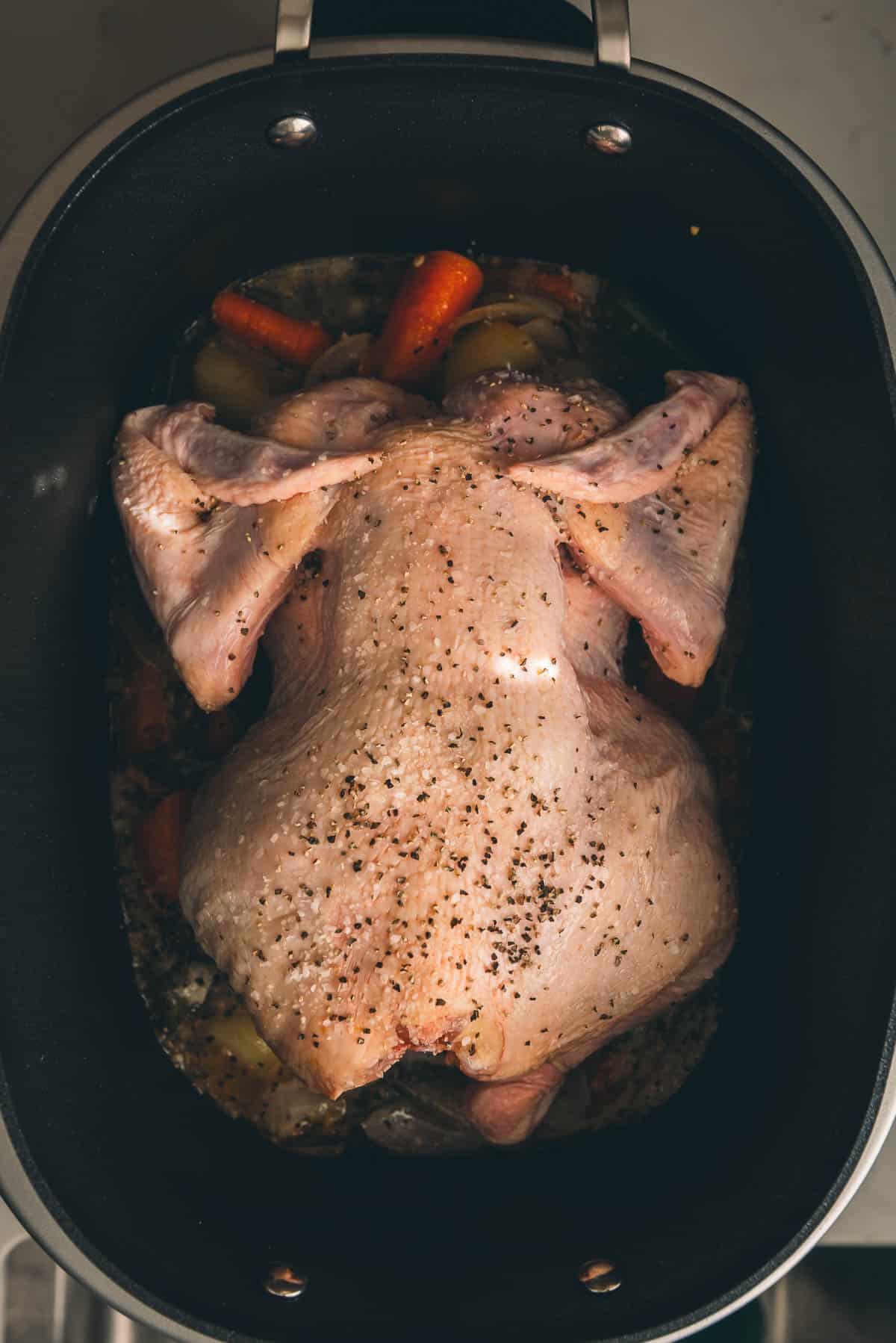A whole chicken is being nestled into a slow cooker over veggies.
