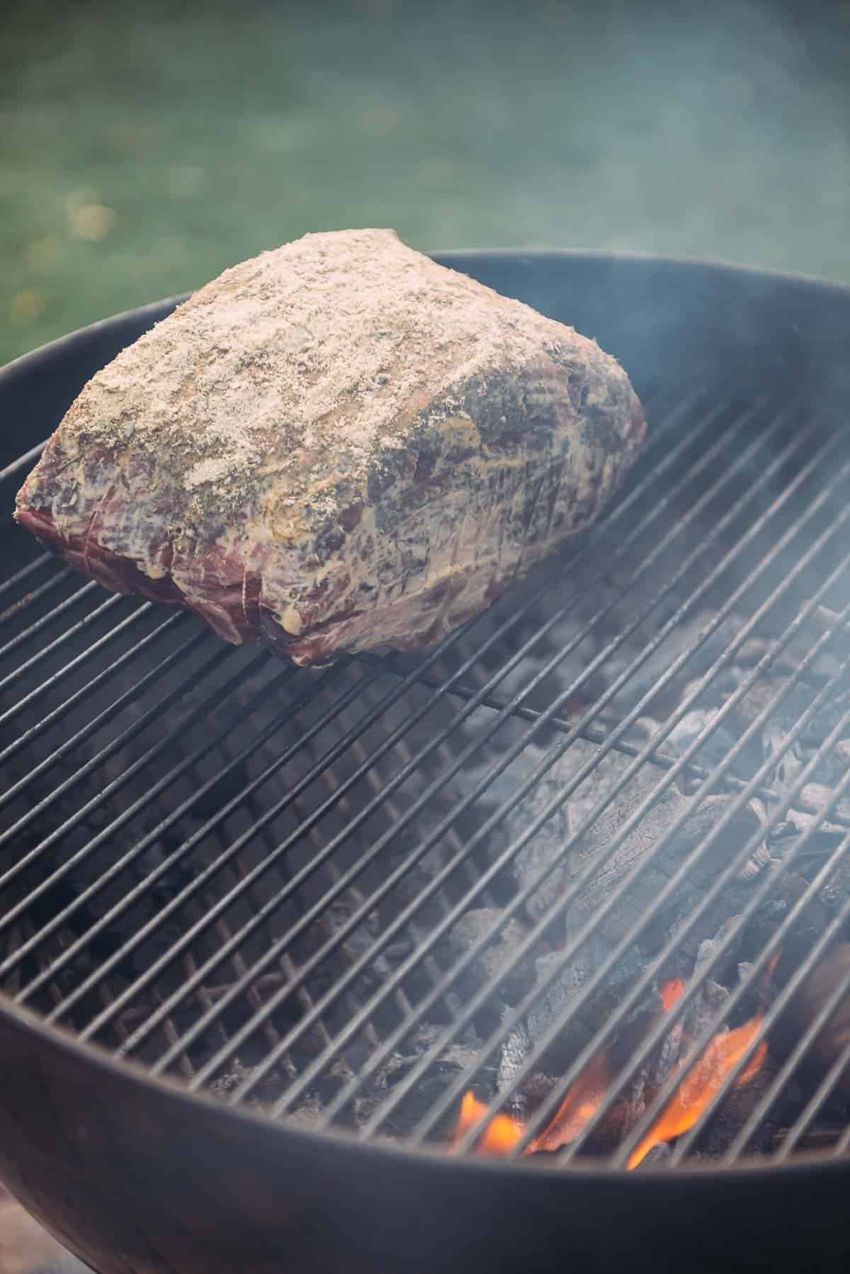 A standing rib roast is being cooked on a grill over indirect heat. 