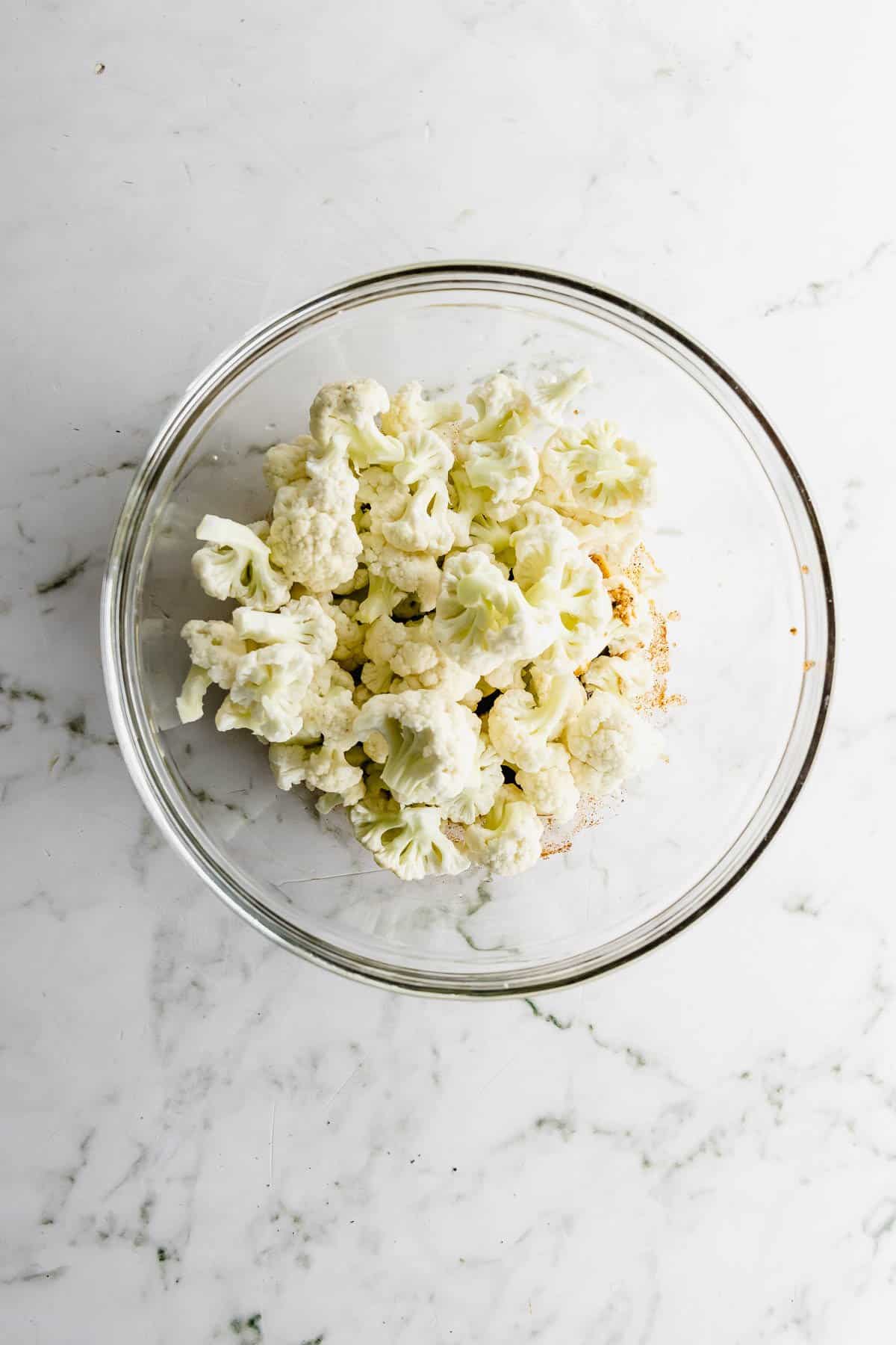 Cauliflower florets in a bowl on a marble countertop.