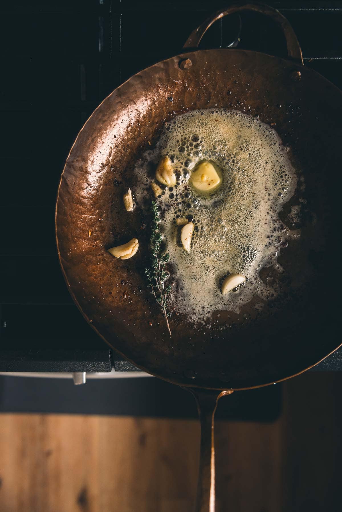 A frying pan with oil and garlic on top of a stove.