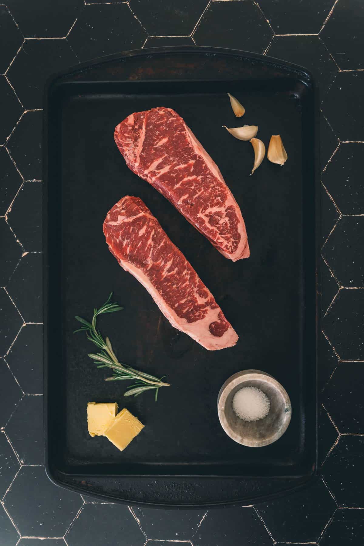 Strip steaks on a black tray.