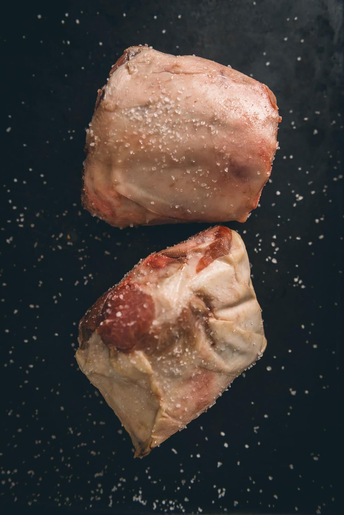 Two salted pork shanks on a black surface.