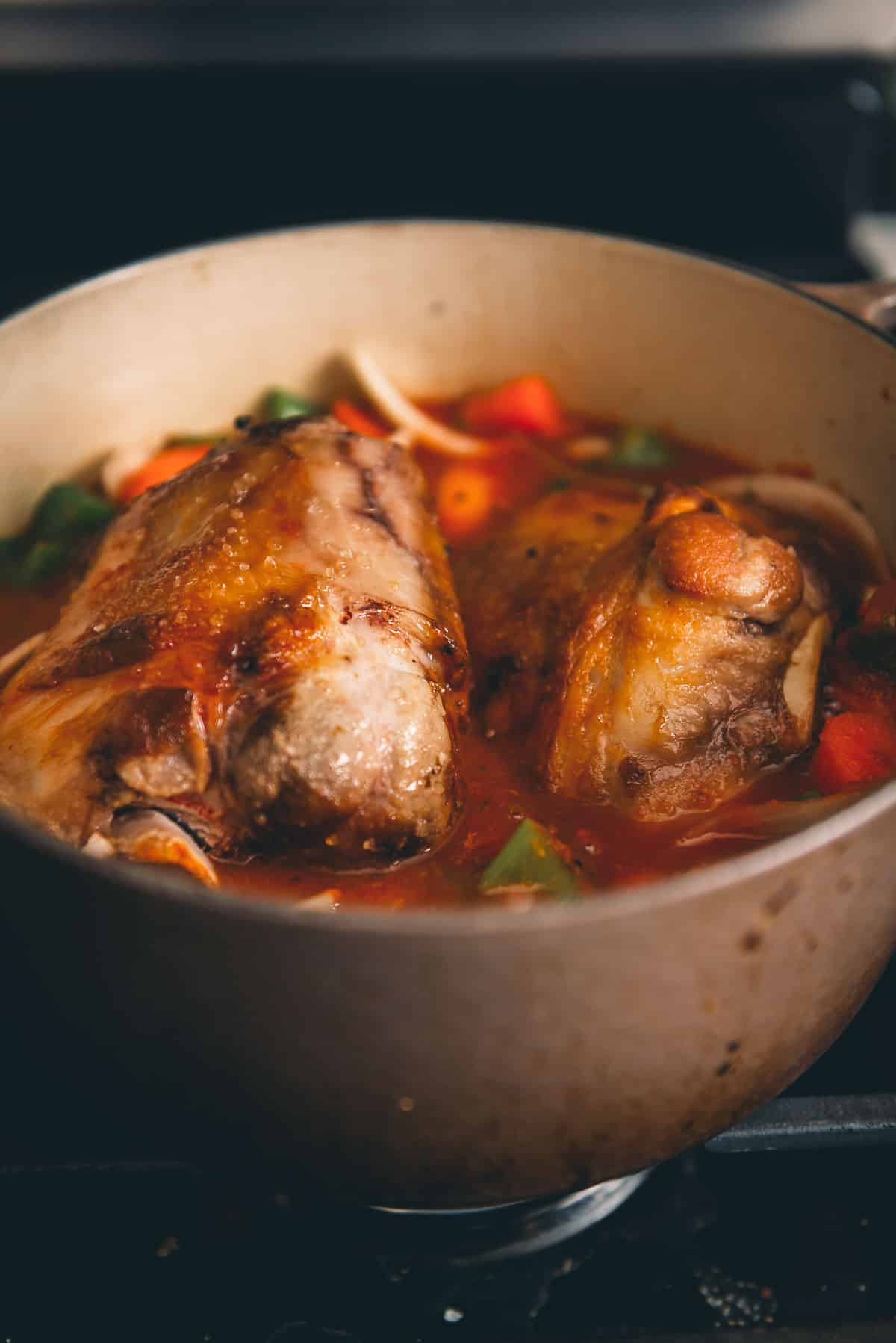 Browned pork shanks nestled into the braising liquid with veggies in a Dutch oven.