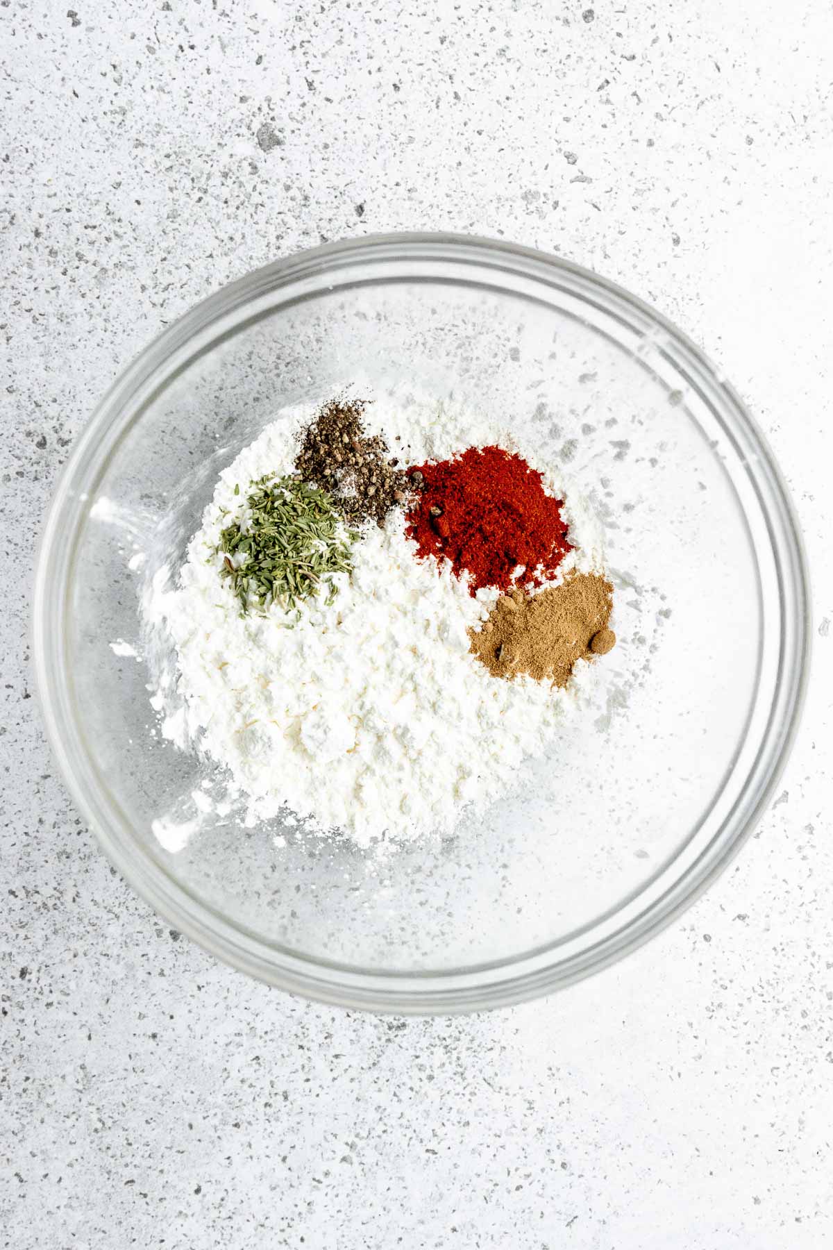 A glass bowl with spices and seasonings on a white surface.