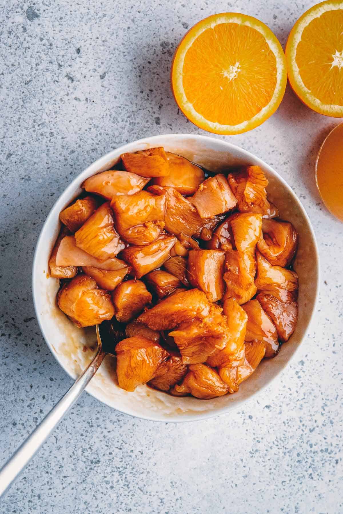 A bowl of chicken with orange slices and a spoon.