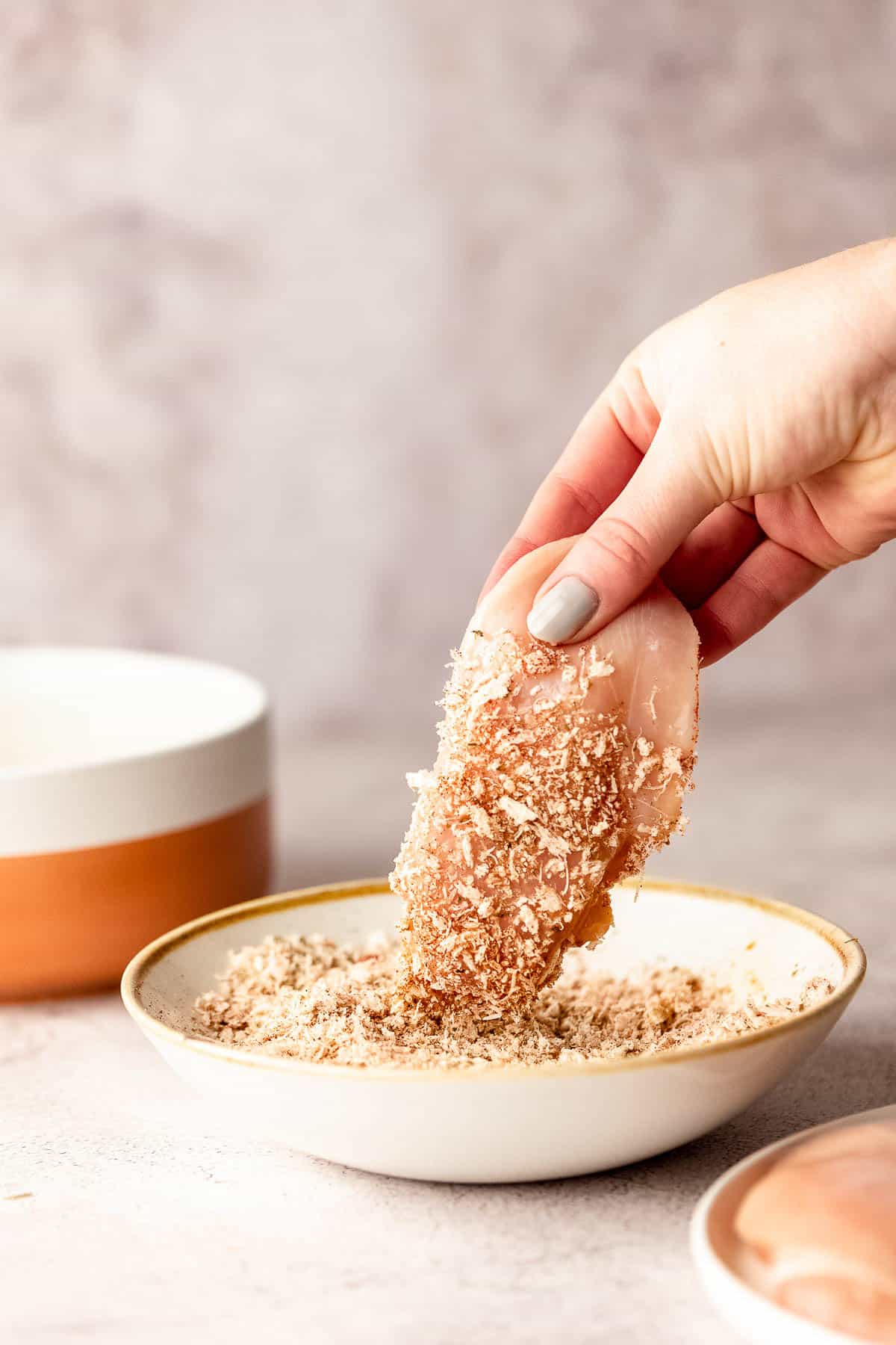 A person dipping chicken breasts in panko bread crumbs.