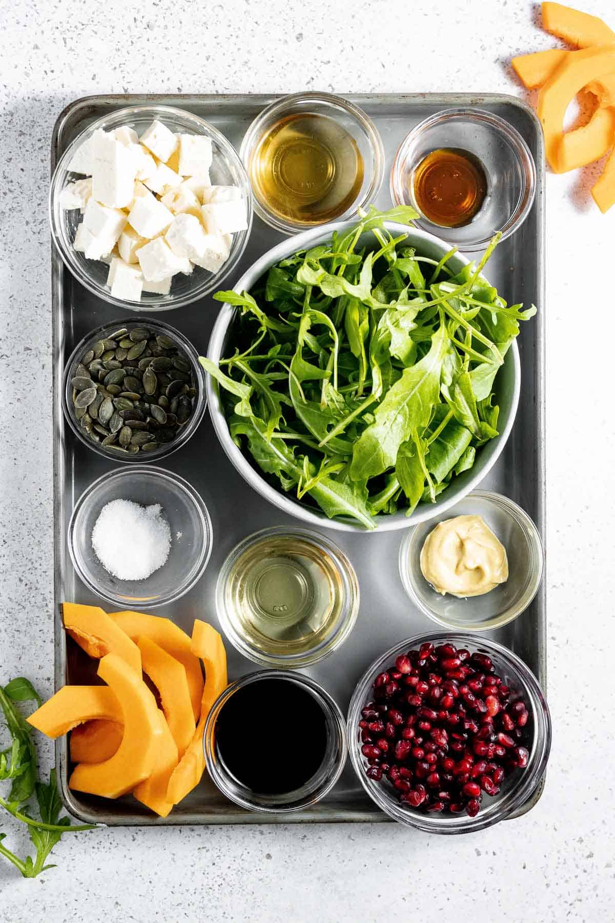 A tray of ingredients for a roasted squash, with arugula salad and pomegranate.