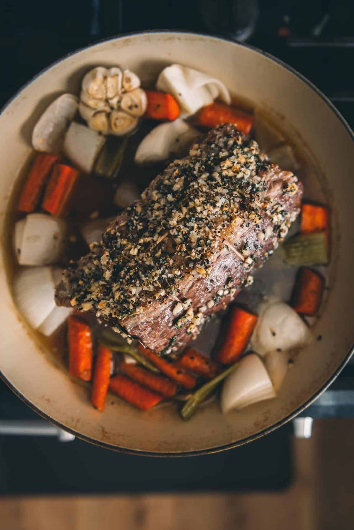 A Dutch oven full of meat and vegetables on a stove.