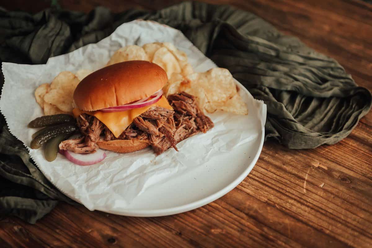 A pulled pork sandwich with potato chips on a white plate.