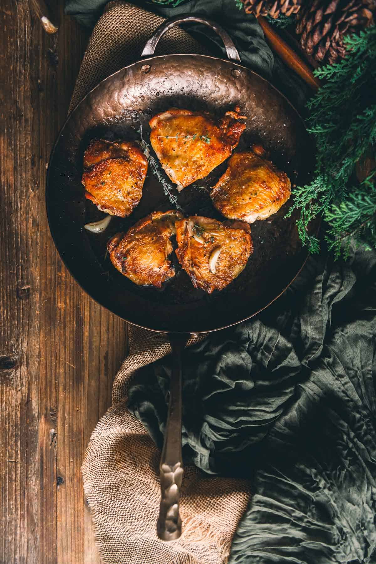 Pan seared chicken in a frying pan on a wooden table.
