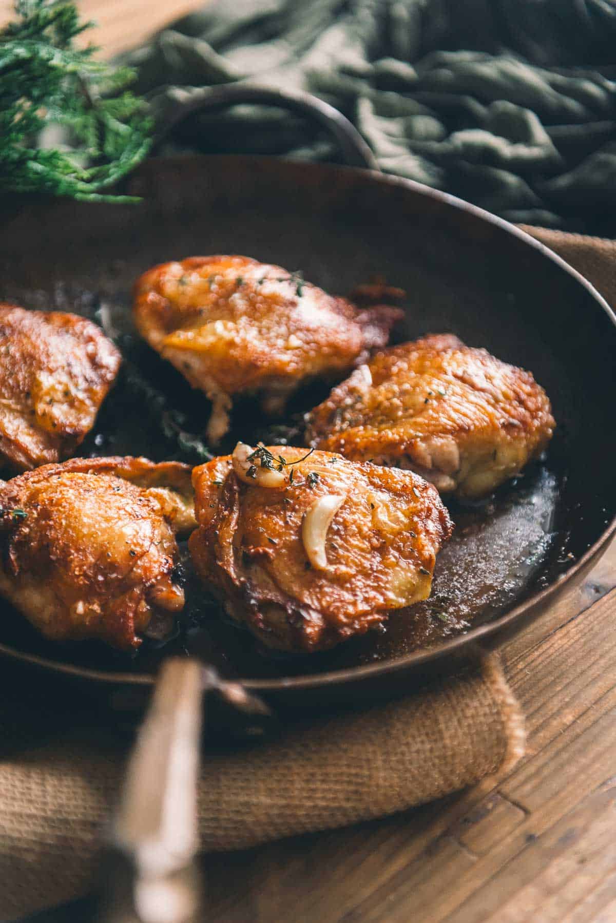 Pan seared chicken thighs in a skillet on a wooden table.