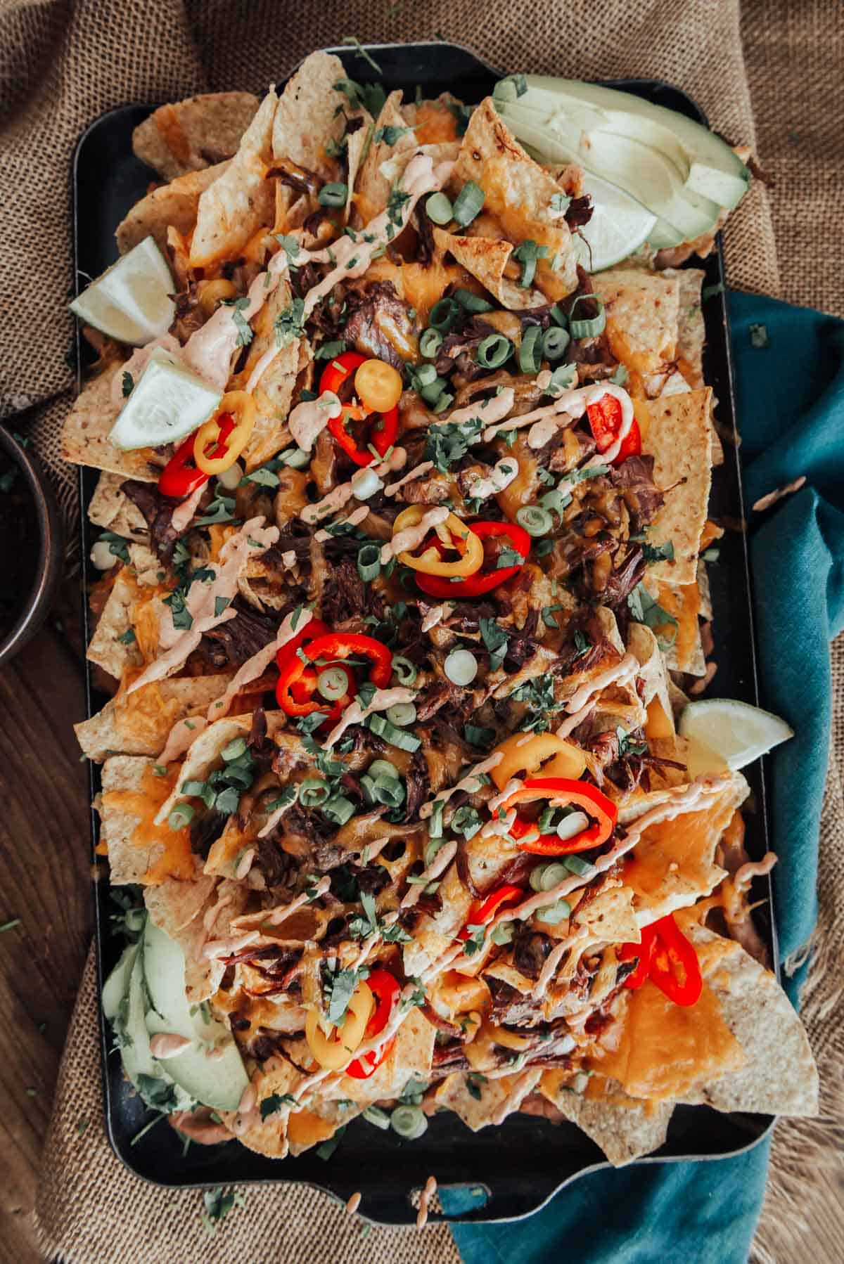 Loaded birria Nachos on a tray with toppings.