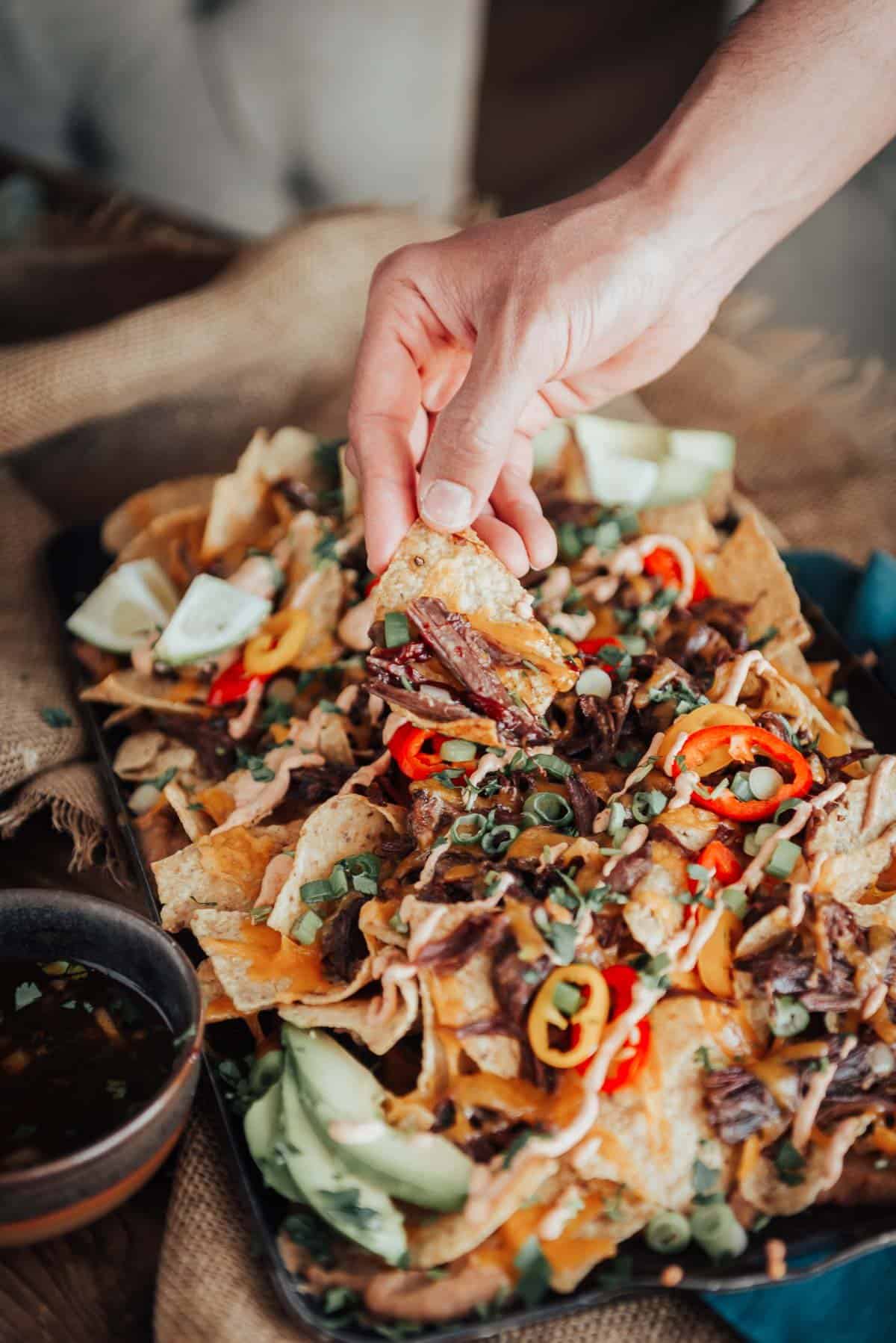 A person grabbing nachos from a tray.