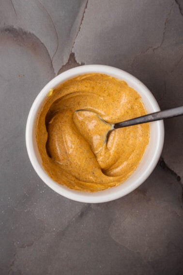 A bowl of Turmeric aioli with a spoon in it.