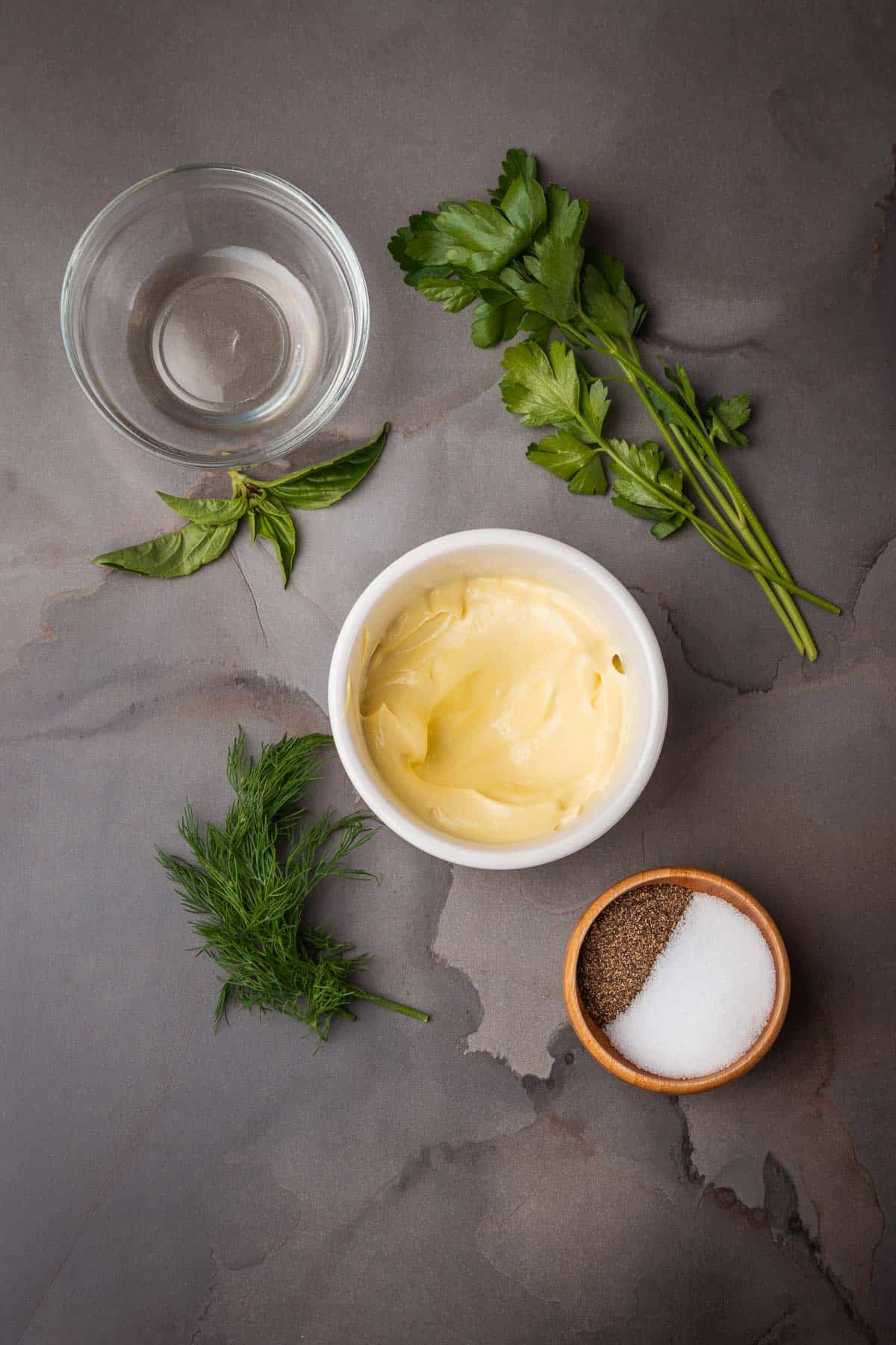 A bowl of aioli, parsley, and salt on a gray background.