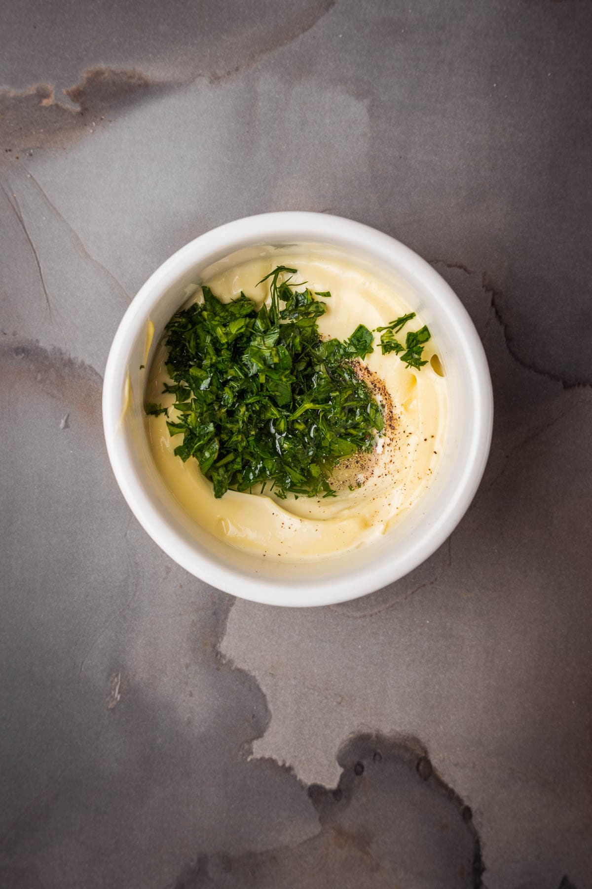 A bowl of aioli with herbs like parsley in it.