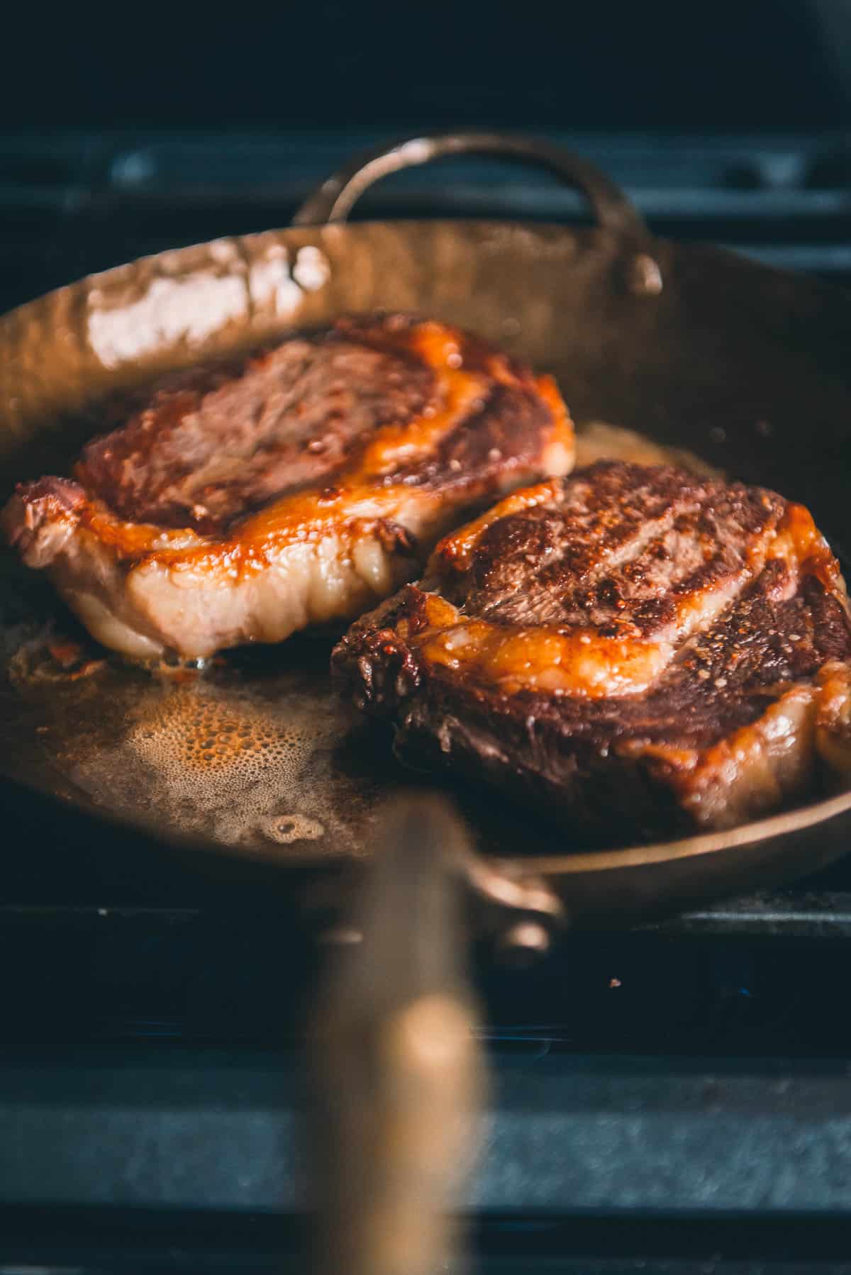 Two steaks in a frying pan on a stove.