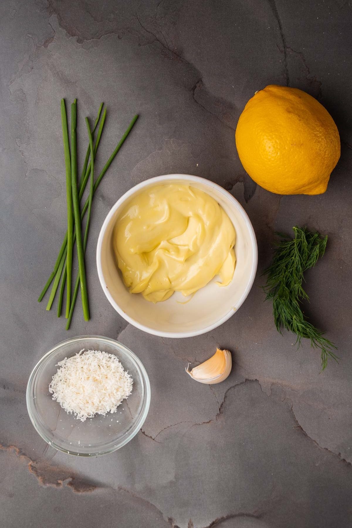 The ingredients for a lemon aioli on a grey background.
