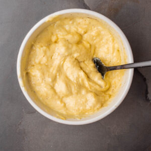 A bowl of yellow roasted squash aioli with a spoon in it.