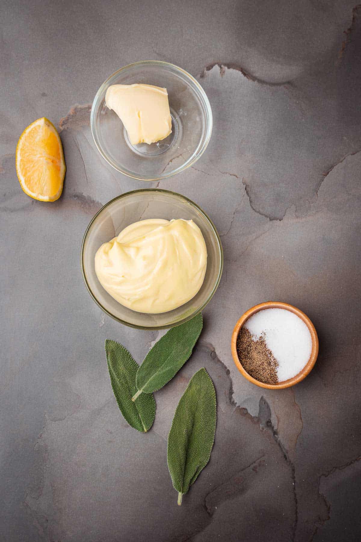 A bowl of aioli, lemon juice, and a slice of orange on a gray background.