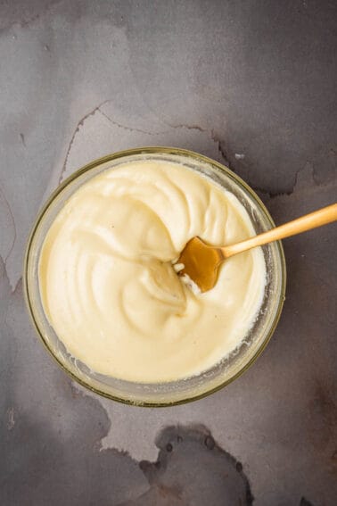 Sage aioli in a glass bowl with a wooden spoon.