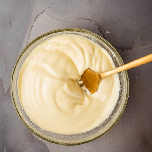 Sage aioli in a glass bowl with a wooden spoon.