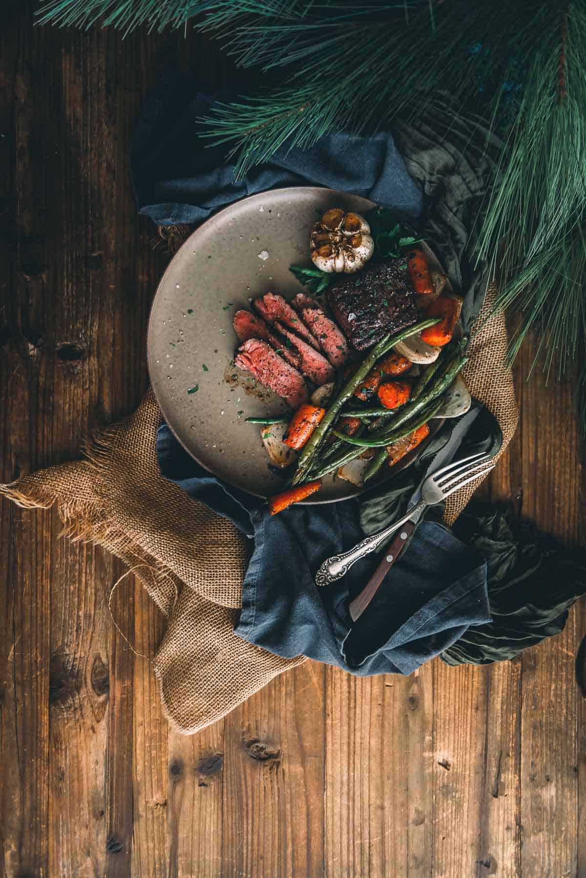 A plate with steak and vegetables on a wooden table.