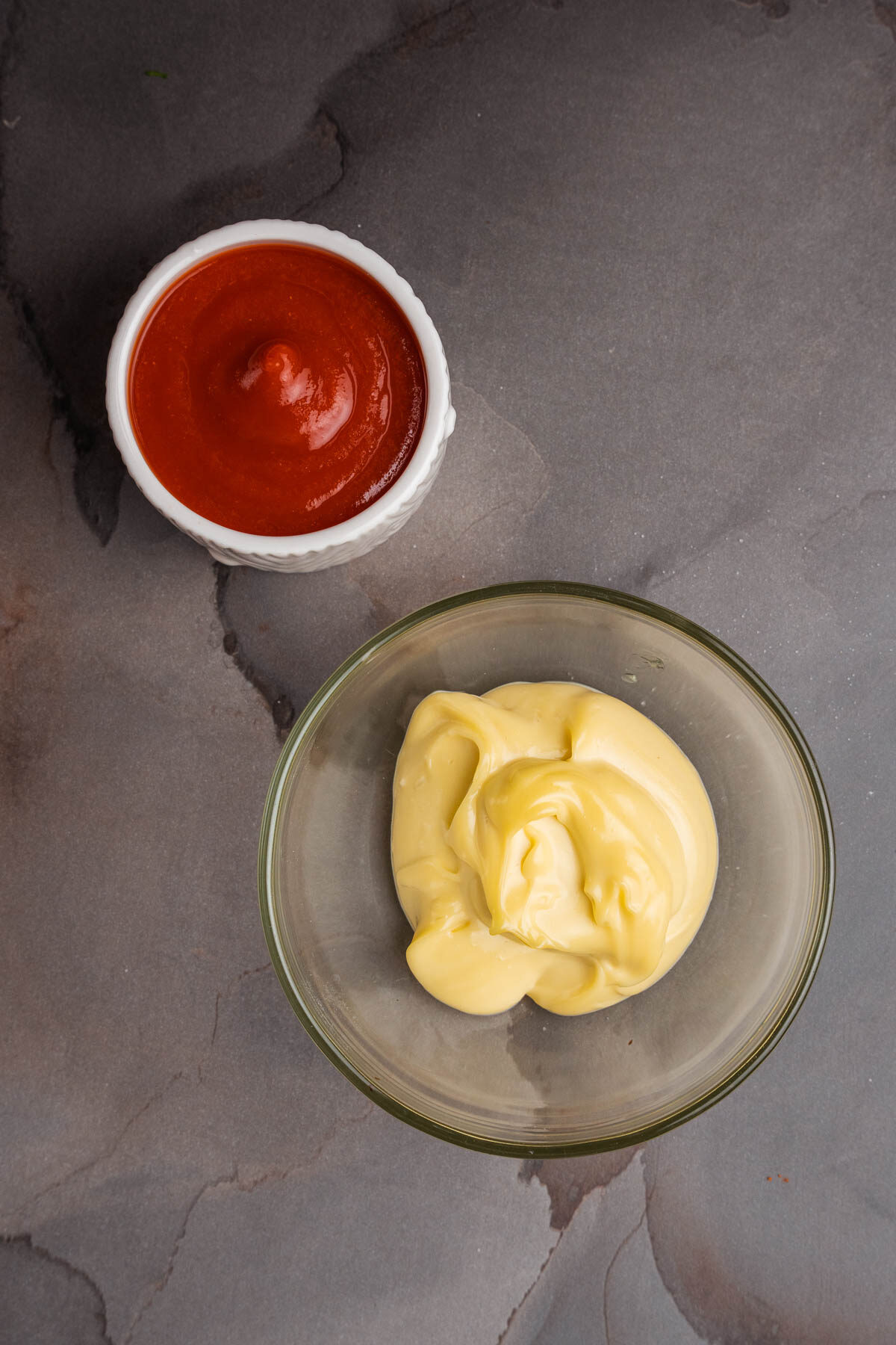 Sriracha and aioli in bowls on a gray surface.