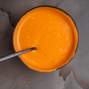 A bowl of sriracha aioli with a spoon in it.