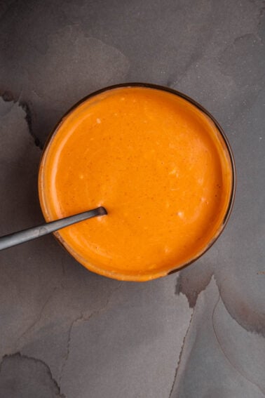 A bowl of sriracha aioli with a spoon in it.