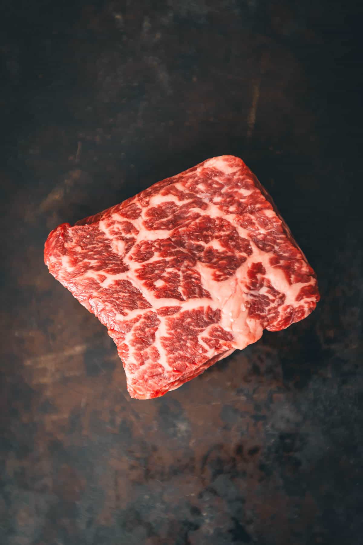 A well marbled of steak on a dark surface.